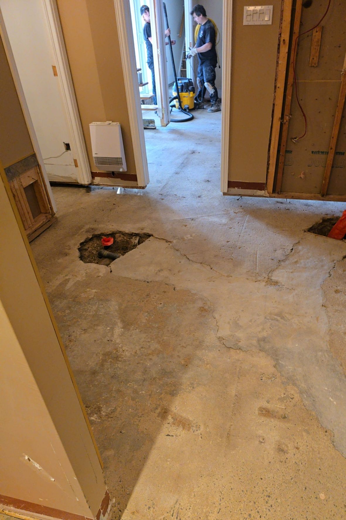 Plancher de sous-sol ouvert avec sections retirées et travailleurs en arrière-plan dans un bâtiment en rénovation  à Québec